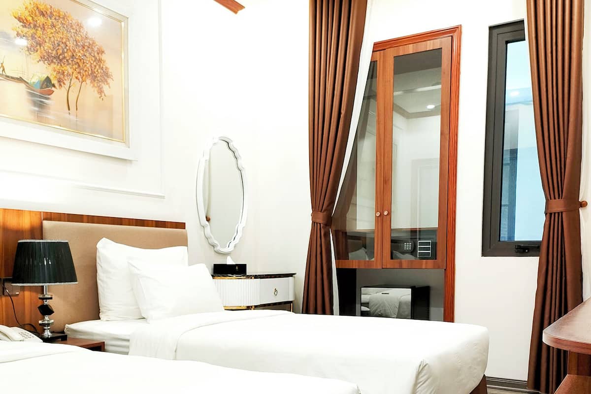 A hotel room with two beds, a desk, a mirror, and a window with curtains.