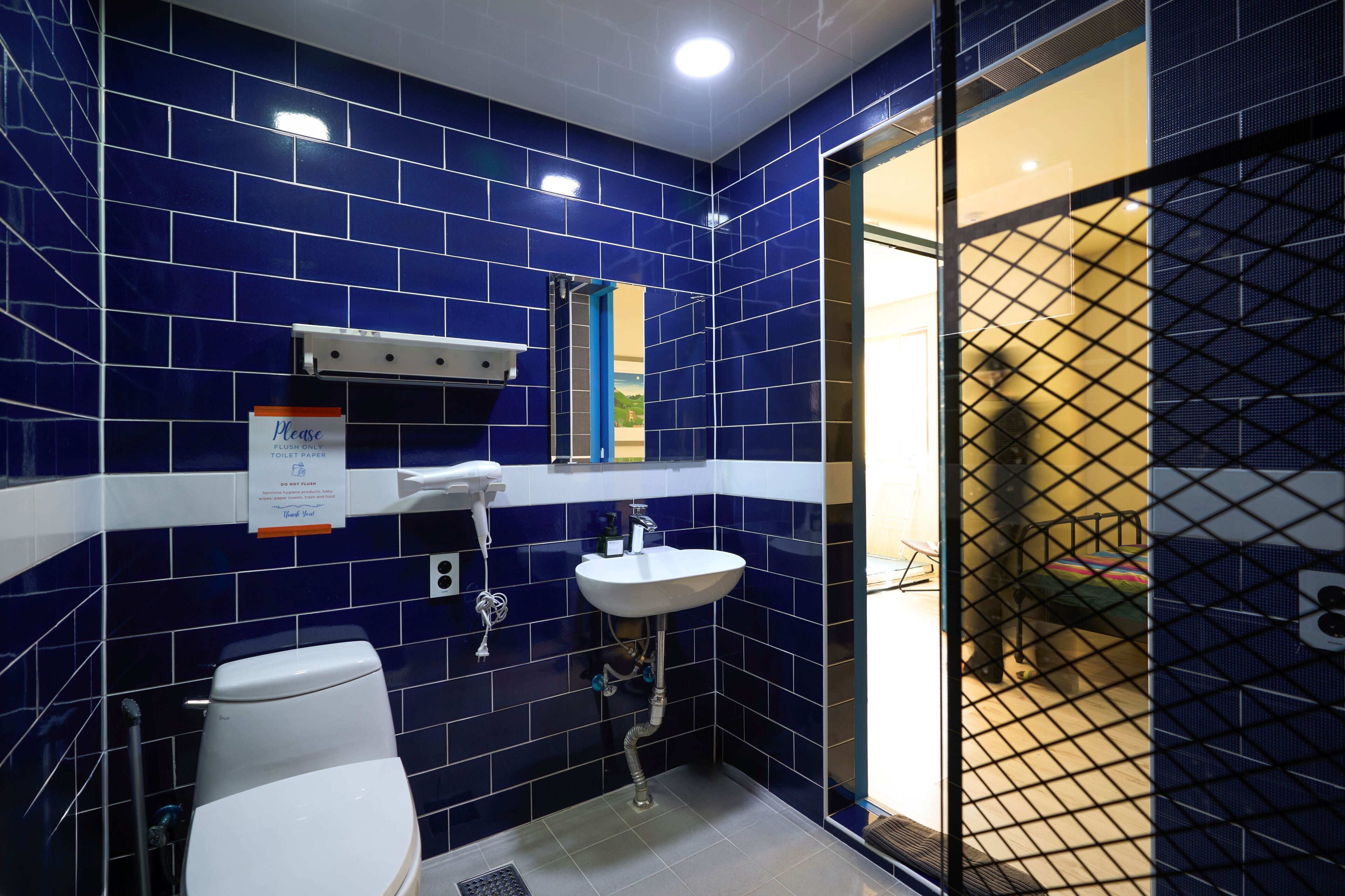 Une salle de bain avec des carreaux bleus, un lavabo blanc, des toilettes et un espace douche.