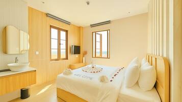 Un dormitorio moderno con piso de madera, una cama blanca con un cartel que dice 'WELCOME', cabecera de madera, un espejo grande y vista a la playa a través de las ventanas.