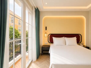 Habitación de hotel con una cama grande, una mesita de noche, una lámpara y vistas al exterior.