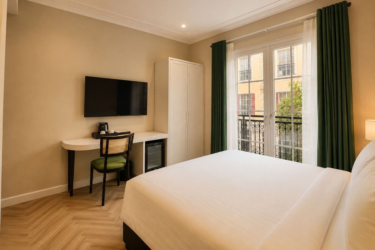 A hotel room with a bed, a desk with a chair, a television, and a window with curtains.