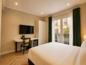 Una habitación de hotel con una cama, un escritorio con una silla, un televisor y una ventana con cortinas.