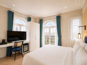 A hotel room with a bed, a desk with a television, a chair, a wardrobe, and a balcony with curtains. - HAN Sunset Milan Hotel & Spa (Phu Quoc)