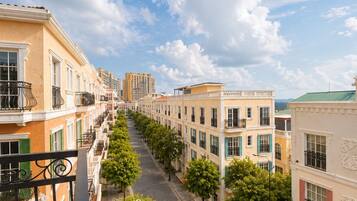 A row of buildings with balconies, a clear sky, and trees lining the street.