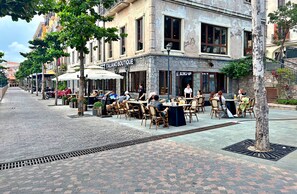 Un café al aire libre con mesas y sillas, un edificio de piedra con un letrero que dice 