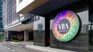 Un edificio moderno con un gran letrero circular que dice "VIA RESIDENCES" y un cartel de bienvenida para KLECITY.
