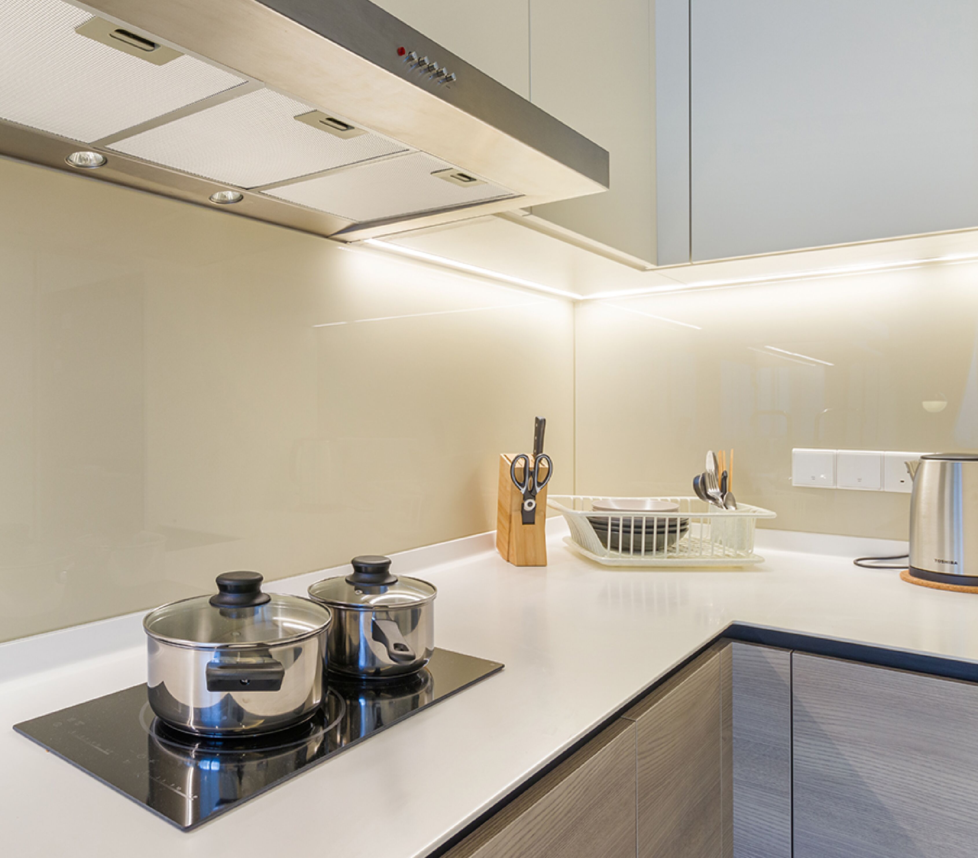 A modern kitchen with a built-in stove, a dish rack, and a kettle on the counter.