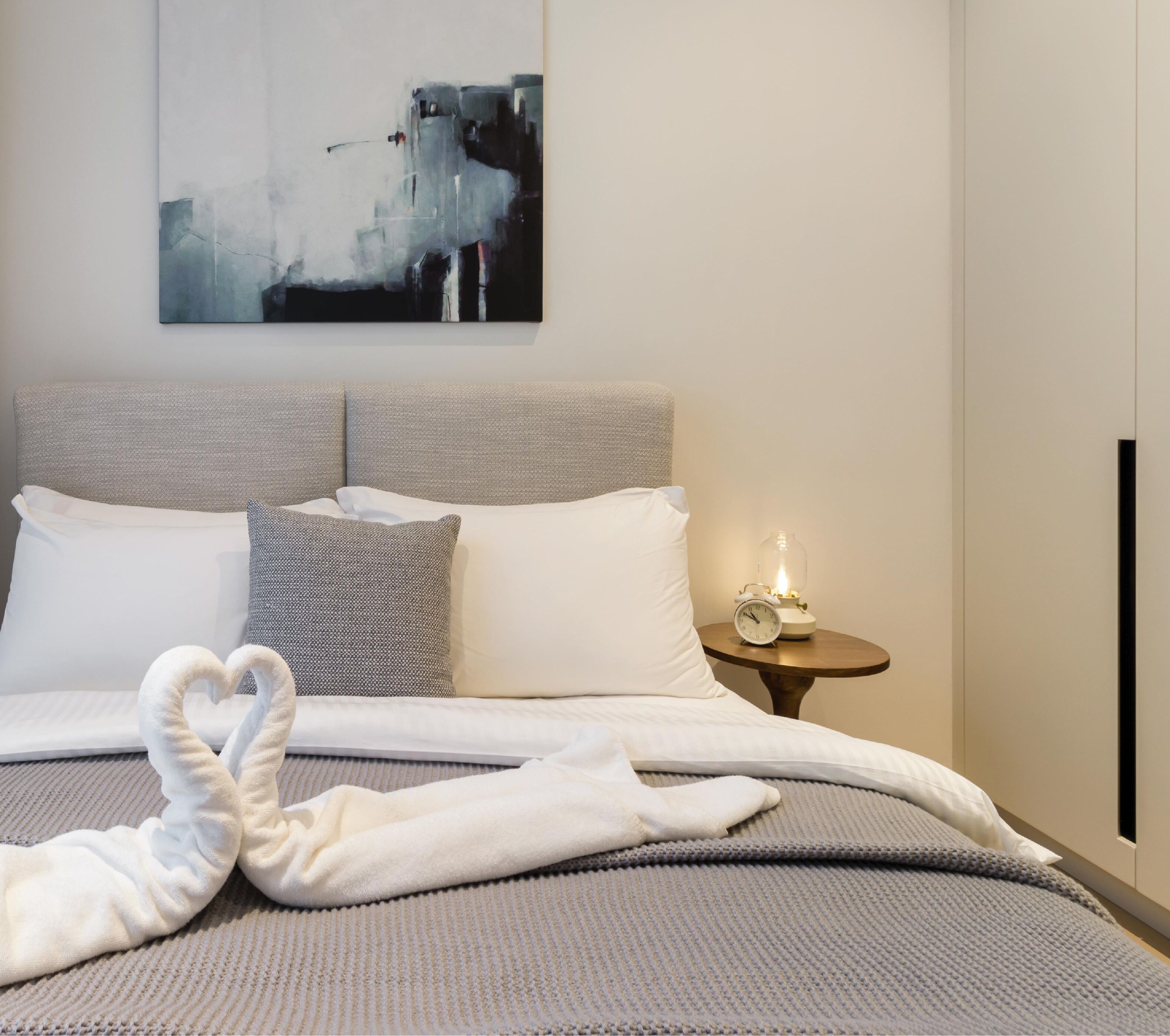 Ein modernes Hotelzimmer mit einem großen Bett, einem Nachttisch mit Lampe und einem Stadtbild an der Wand.