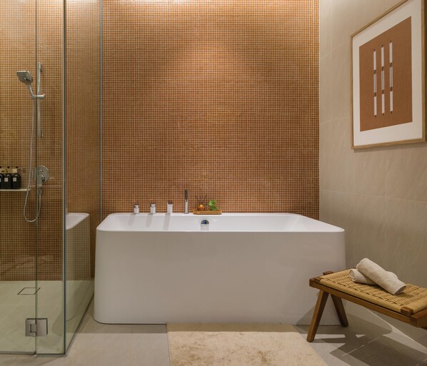Une salle de bain moderne avec une grande baignoire, une douche en verre et un petit banc en bois sur lequel sont posées des serviettes.