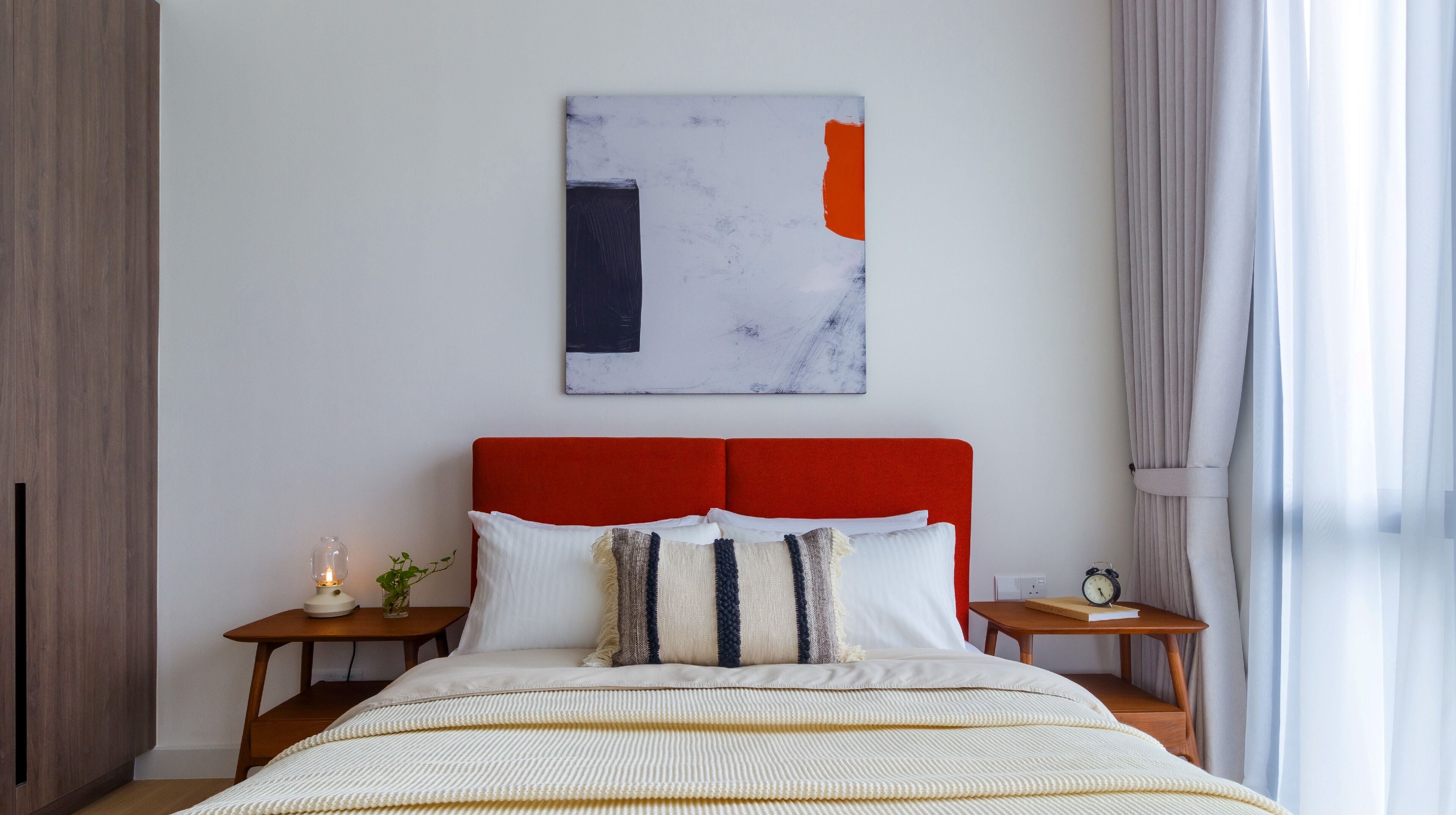 A modern bedroom with a red headboard, a white bedspread, and a minimalist wall art piece.