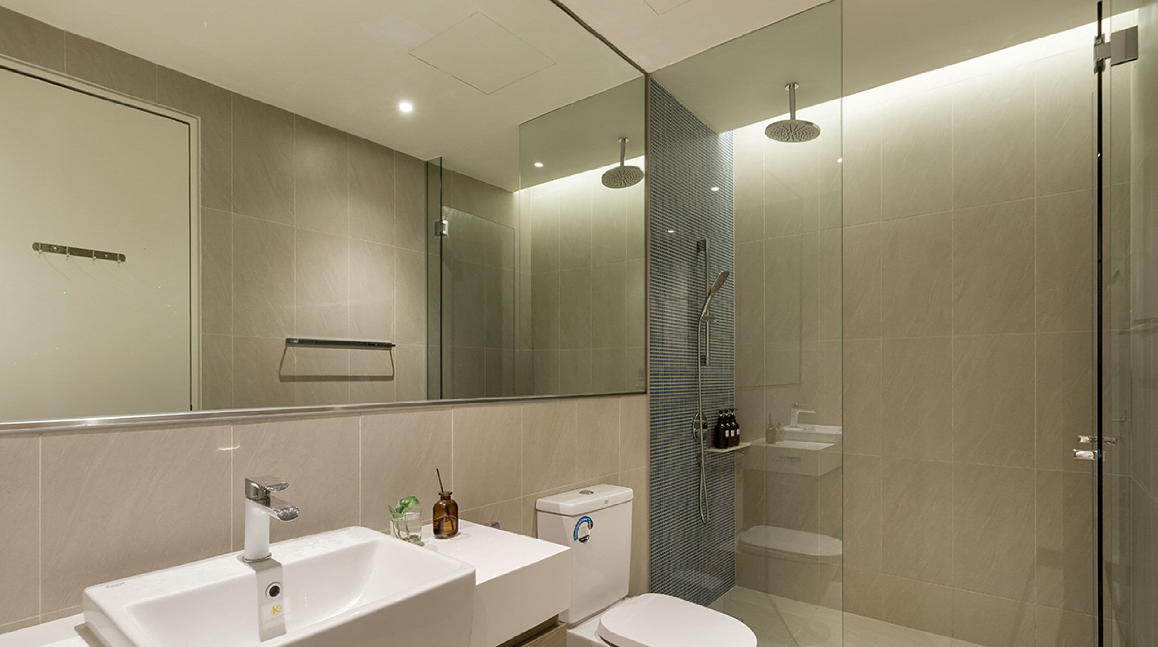 A modern bathroom with a large mirror, a double sink, a toilet, and a shower area.
