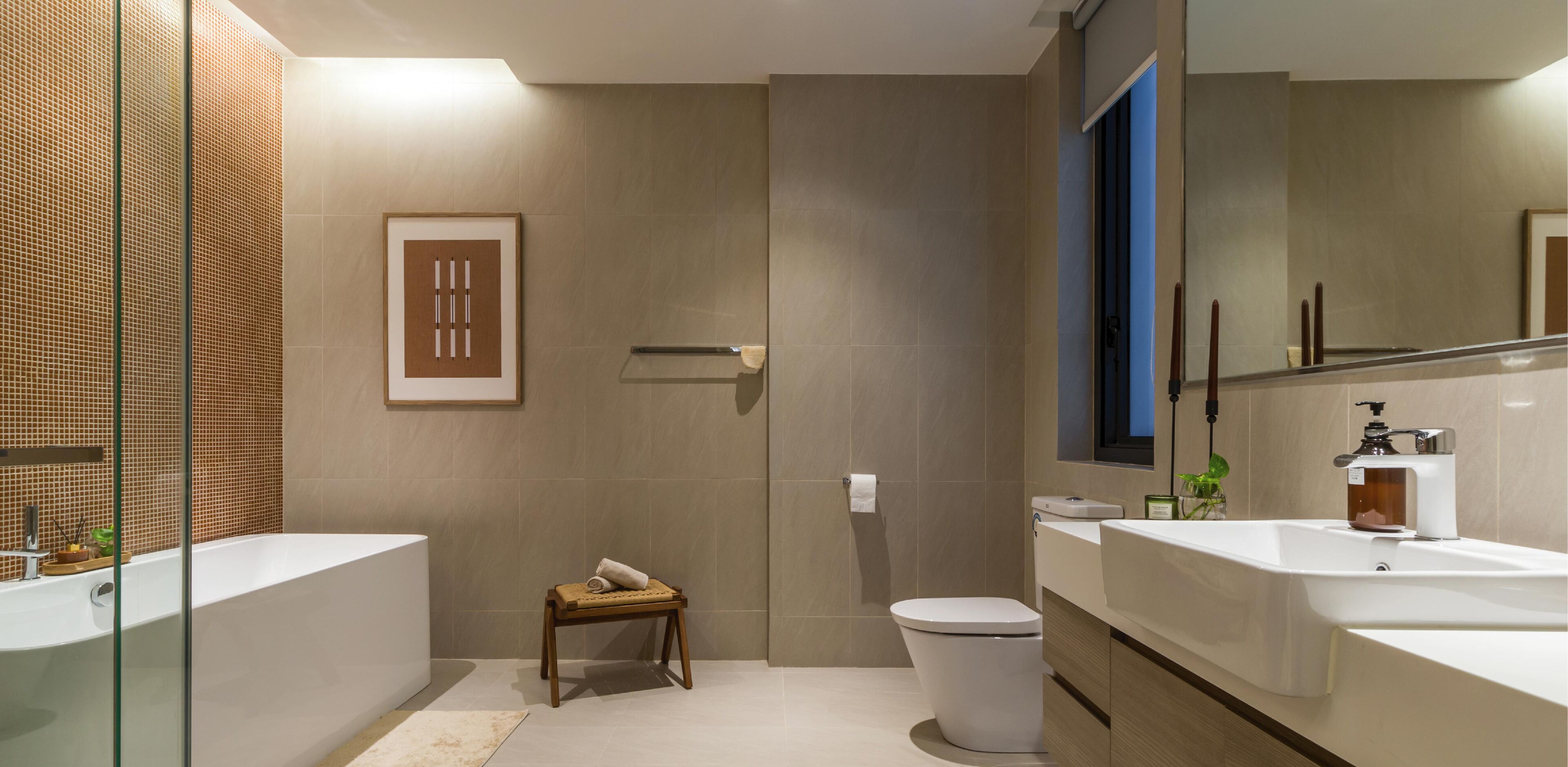 Un baño moderno con bañera, inodoro y lavamanos. Hay un taburete pequeño y un cuadro en la pared.