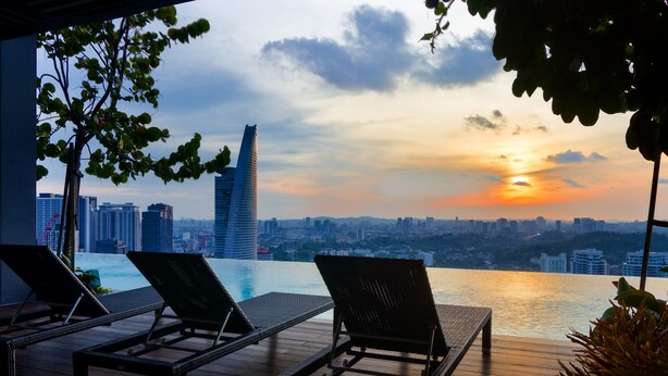 Un área de piscina en la azotea con sillones y vistas a la ciudad al atardecer.