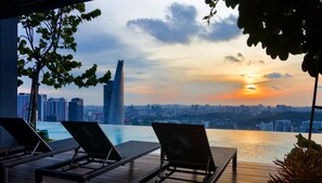 Un espace piscine aménagé sur le toit, avec des chaises longues et une vue sur les toits de la ville au coucher du soleil.