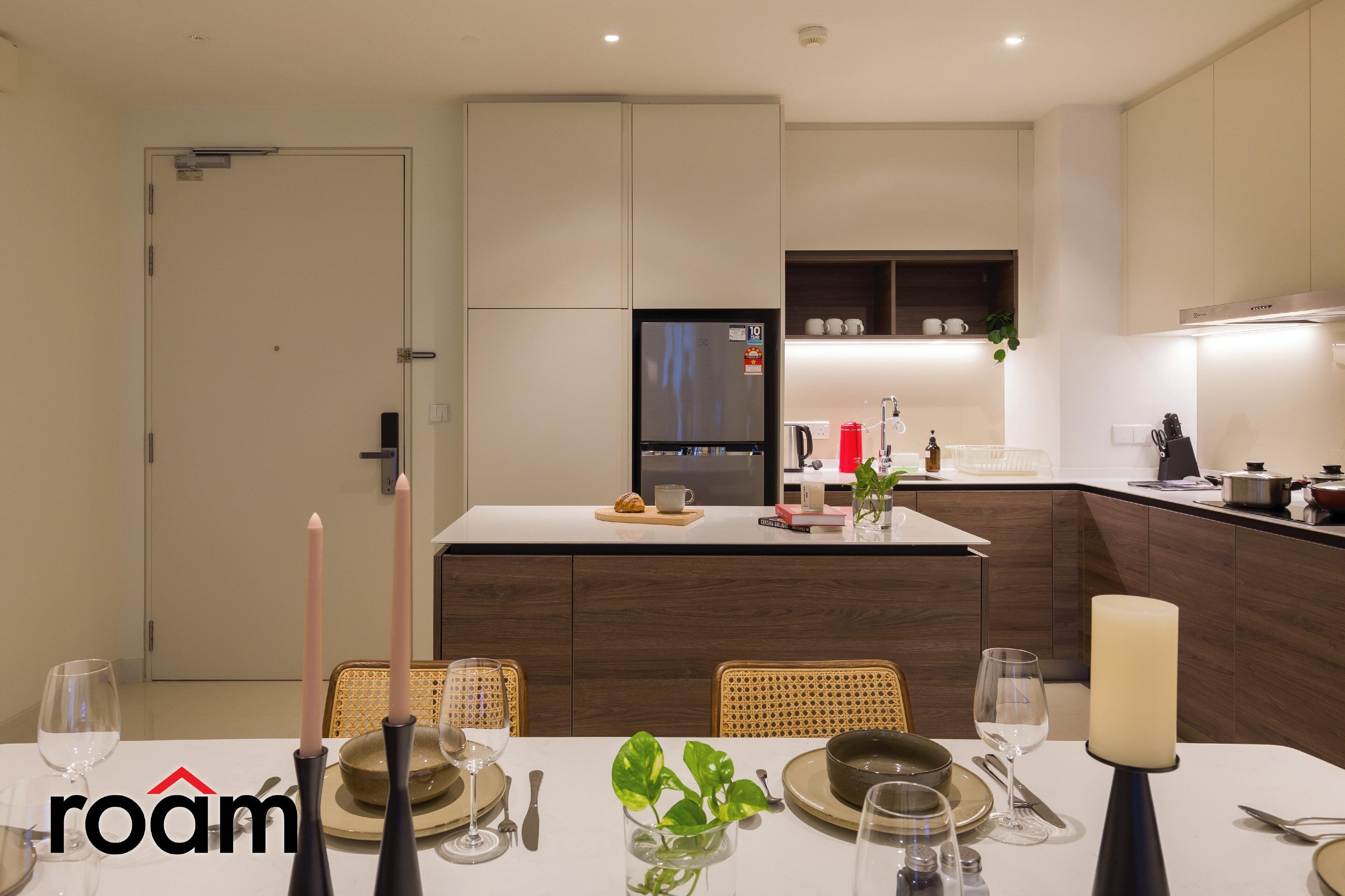 A modern kitchen with a central island, white cabinetry, and a dining area set for four with candles and a plant.