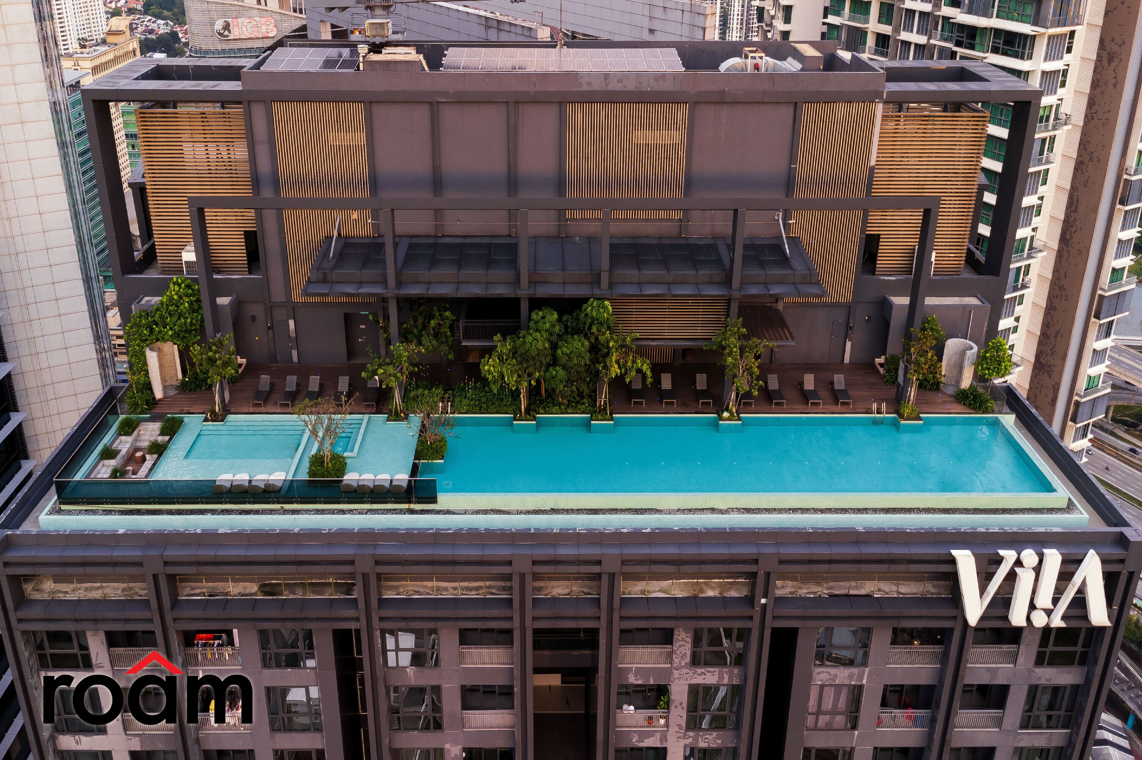 A modern building with a rooftop pool, balconies, and a sign that reads "VIA".