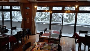A cozy restaurant with wooden interiors and large windows offering a snowy view. - Daisen Basecamp (Daisen)