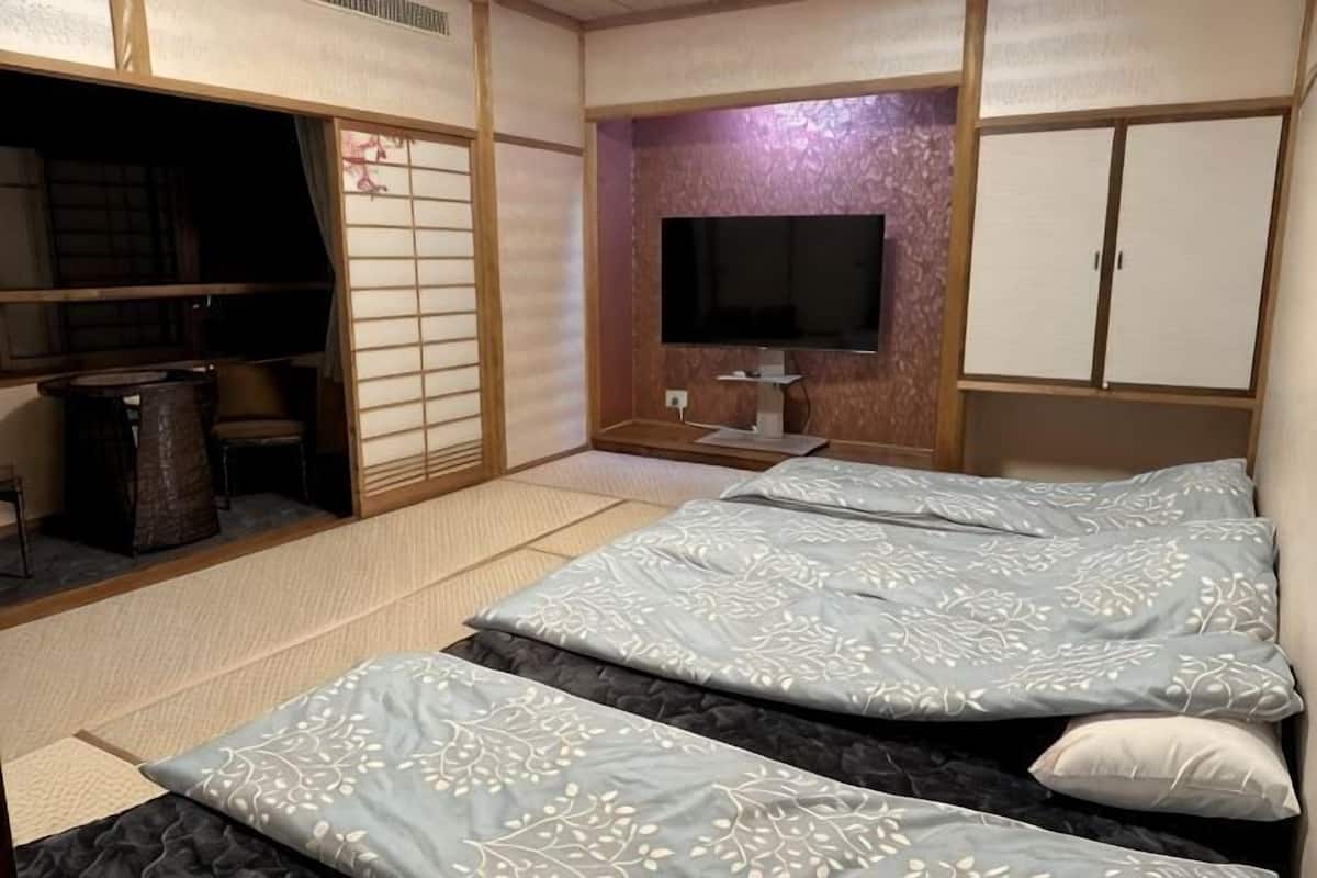 Una habitación tradicional japonesa con suelo de tatami, una cama de madera baja con ropa de cama estampada, un televisor y puertas correderas.