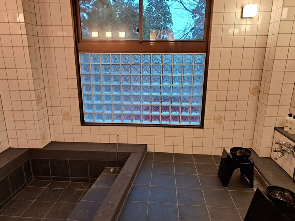 A bathroom with a bathtub, a window with frosted glass, and a shelf with toiletries.
