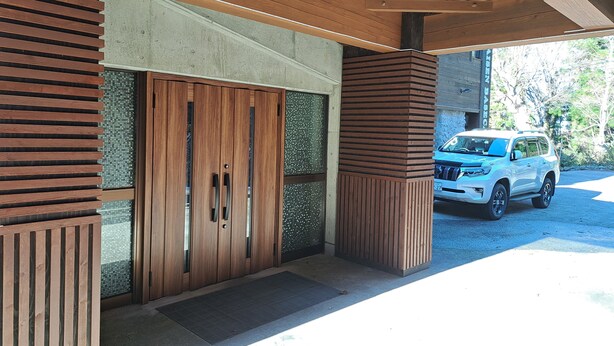 A modern building entrance with a wooden door and a white SUV parked outside. - Daisen Basecamp (Daisen)
