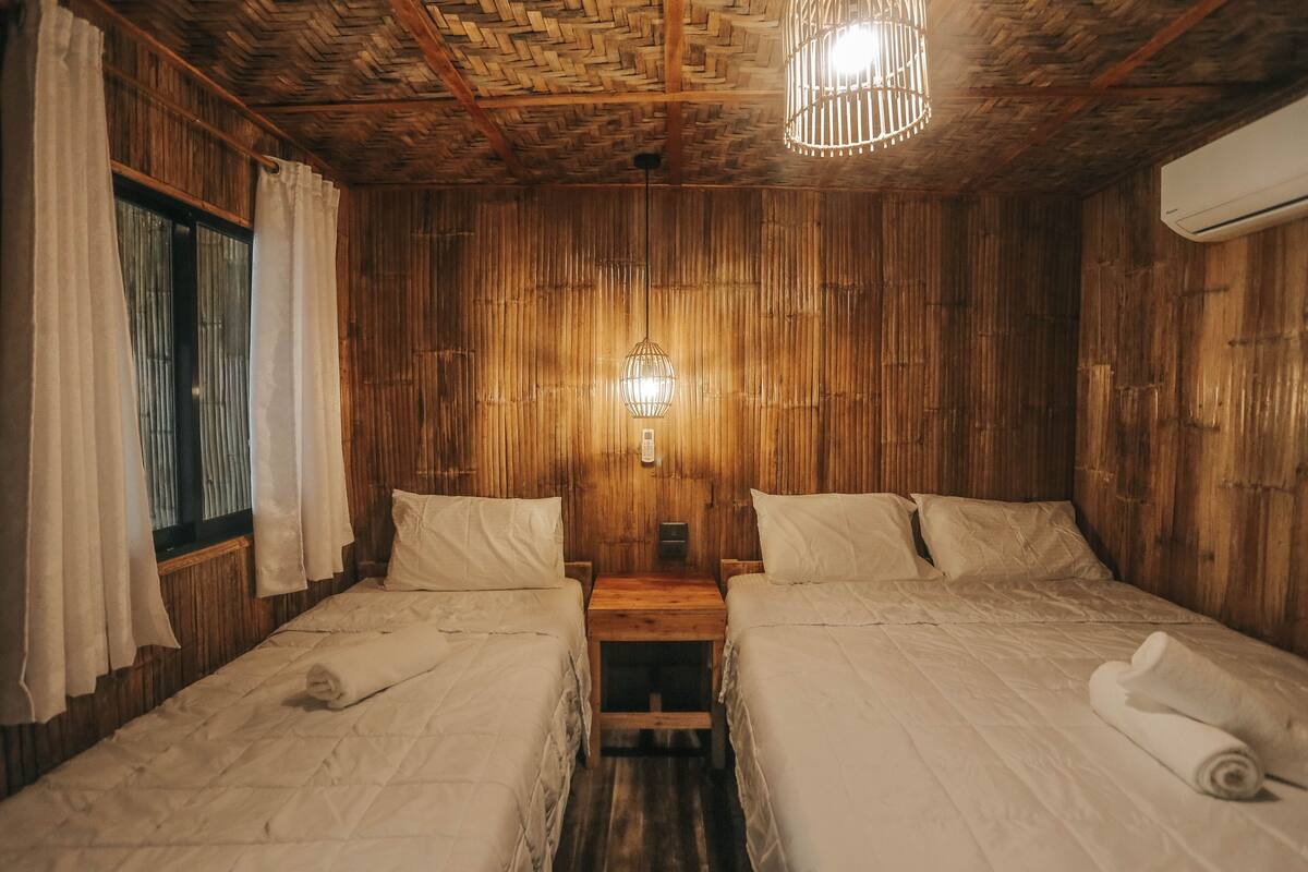 Habitación de madera con dos camas, una mesita de noche, una lámpara de pared y un equipo de aire acondicionado.