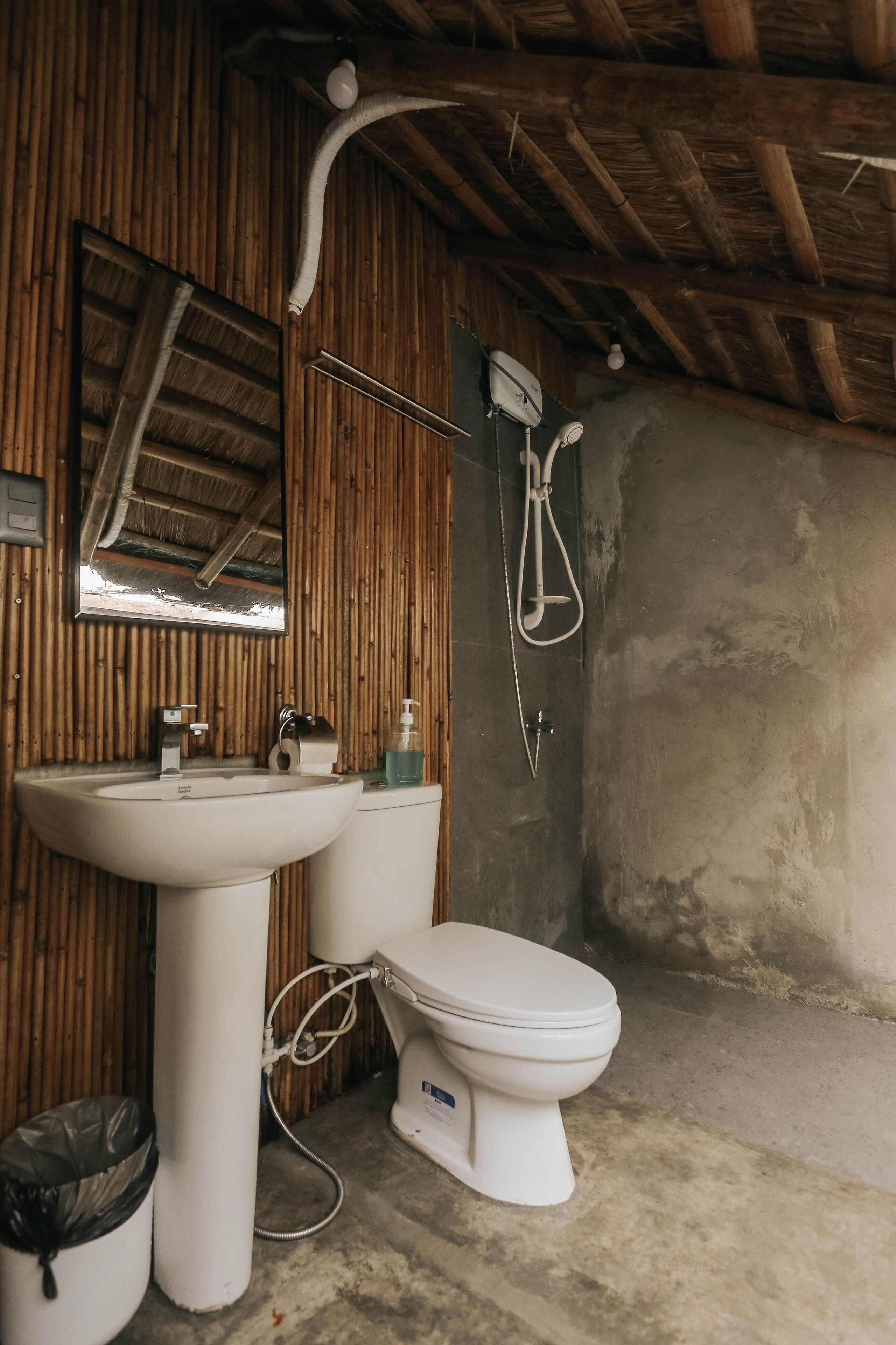 Un baño con pared de madera, lavamanos blanco, inodoro y ducha.