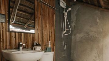 Un baño con pared de madera, lavamanos blanco, inodoro y ducha.