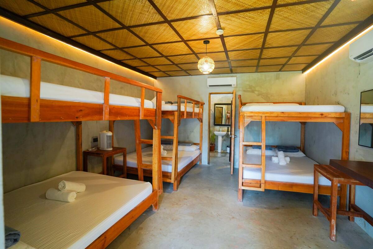 Una habitación tipo dormitorio con literas, una mesita pequeña y una lámpara colgante.
