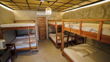 Habitación tipo dormitorio con literas, ventilador de techo y una mesita con una radio.