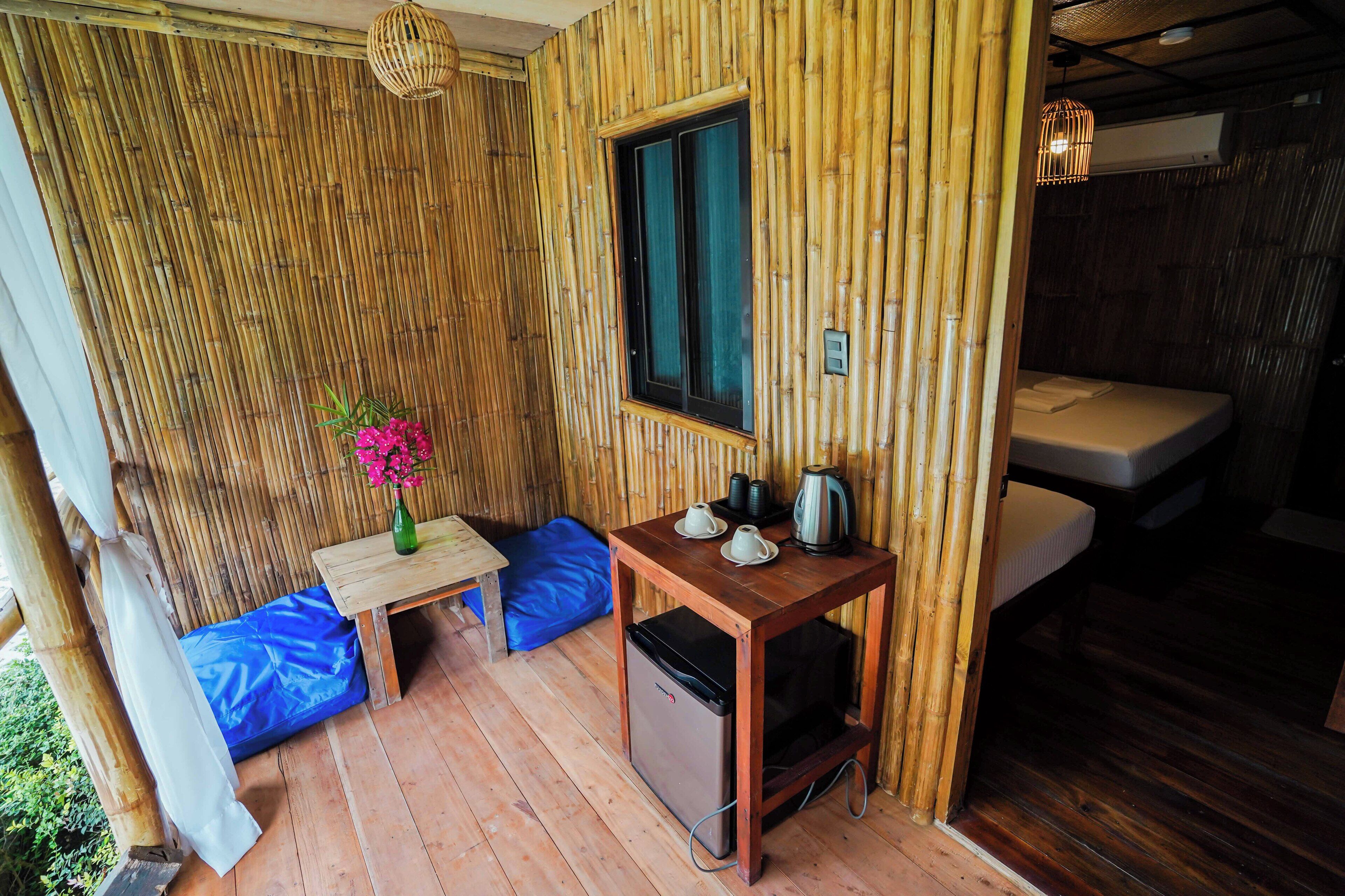 A bamboo-themed room with a bed, a small table with a vase of flowers, and a compact refrigerator.