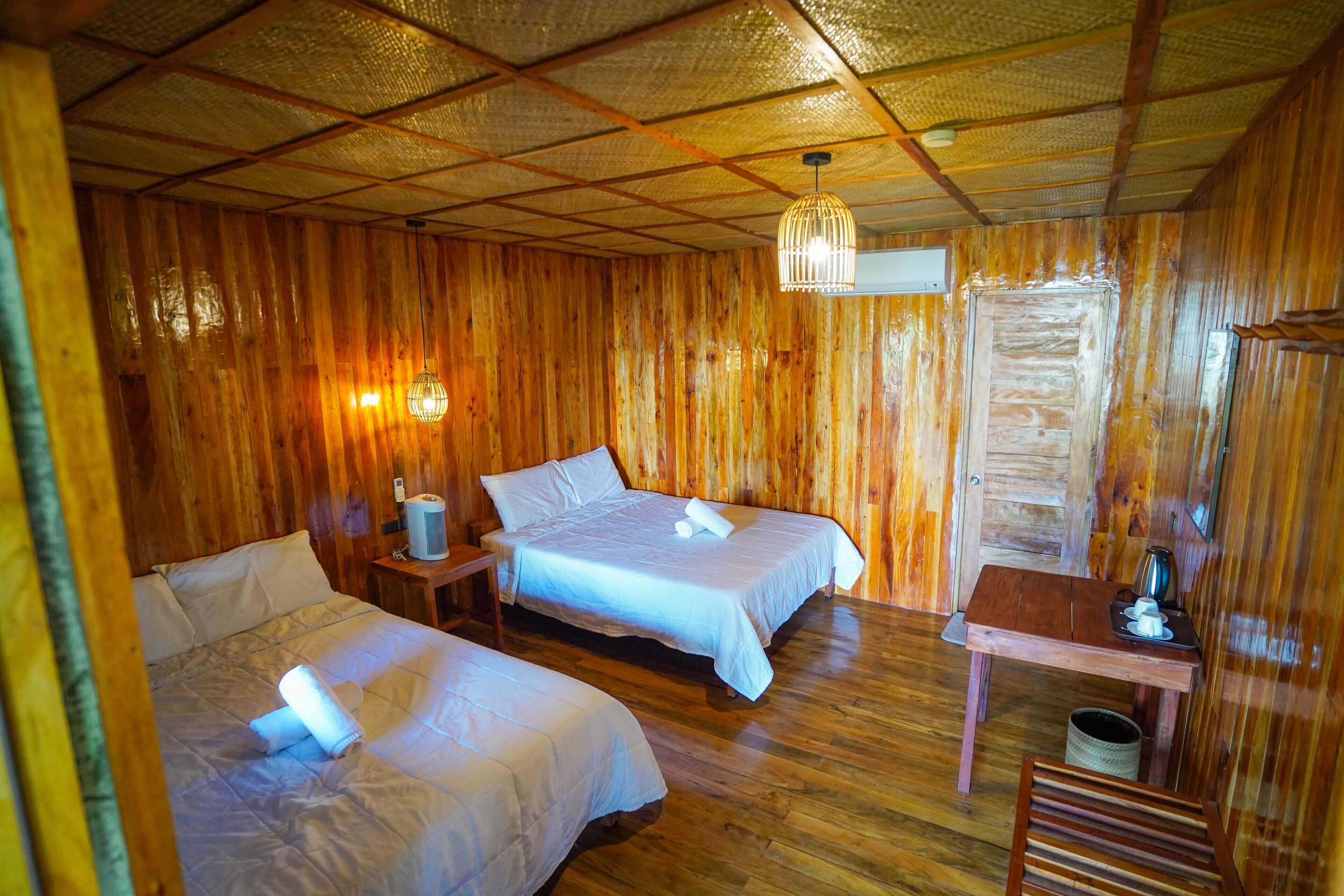 A wooden cabin with two beds, a small table with a kettle, and a hanging light fixture.