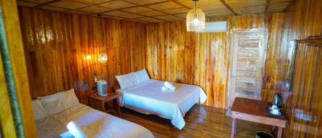 A wooden cabin with two beds, a small table with a kettle, and a hanging light fixture.