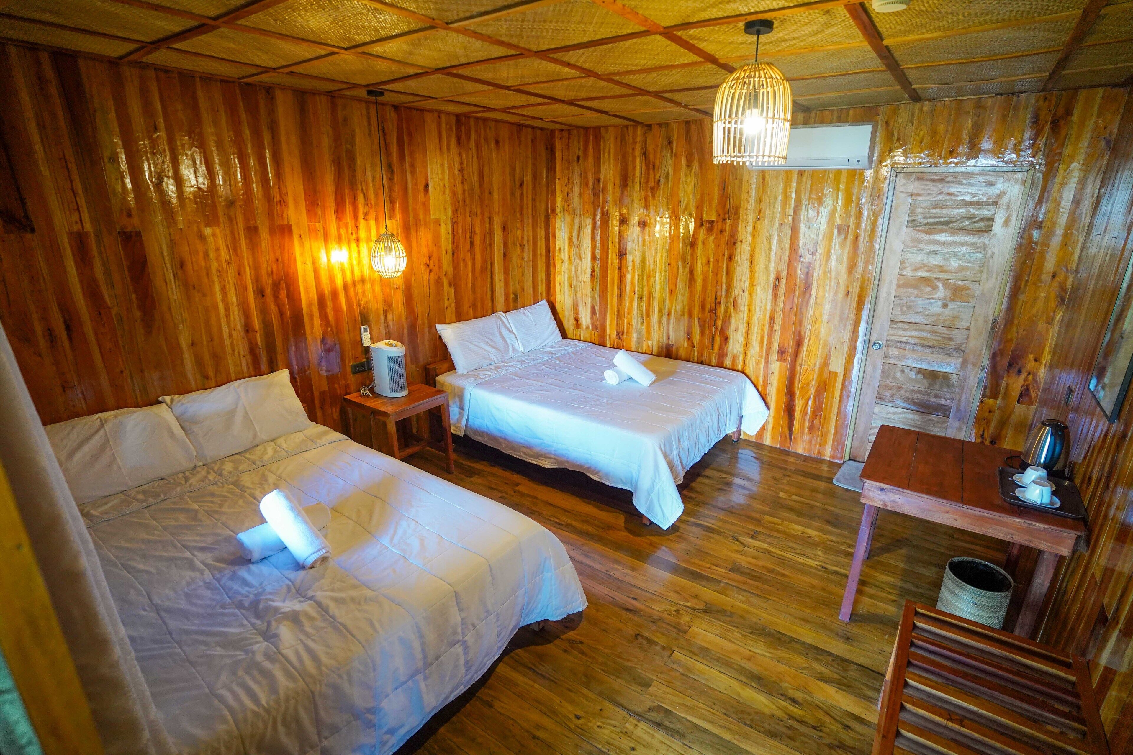 Habitación de cabaña de madera con dos camas, una mesita pequeña y una lámpara colgante.