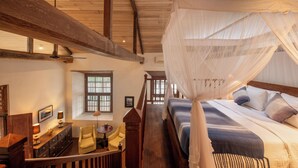 A bedroom with a canopy bed, wooden beams, a desk with a chair, and a window with barred glass. - 32 Middle Street (Galle)