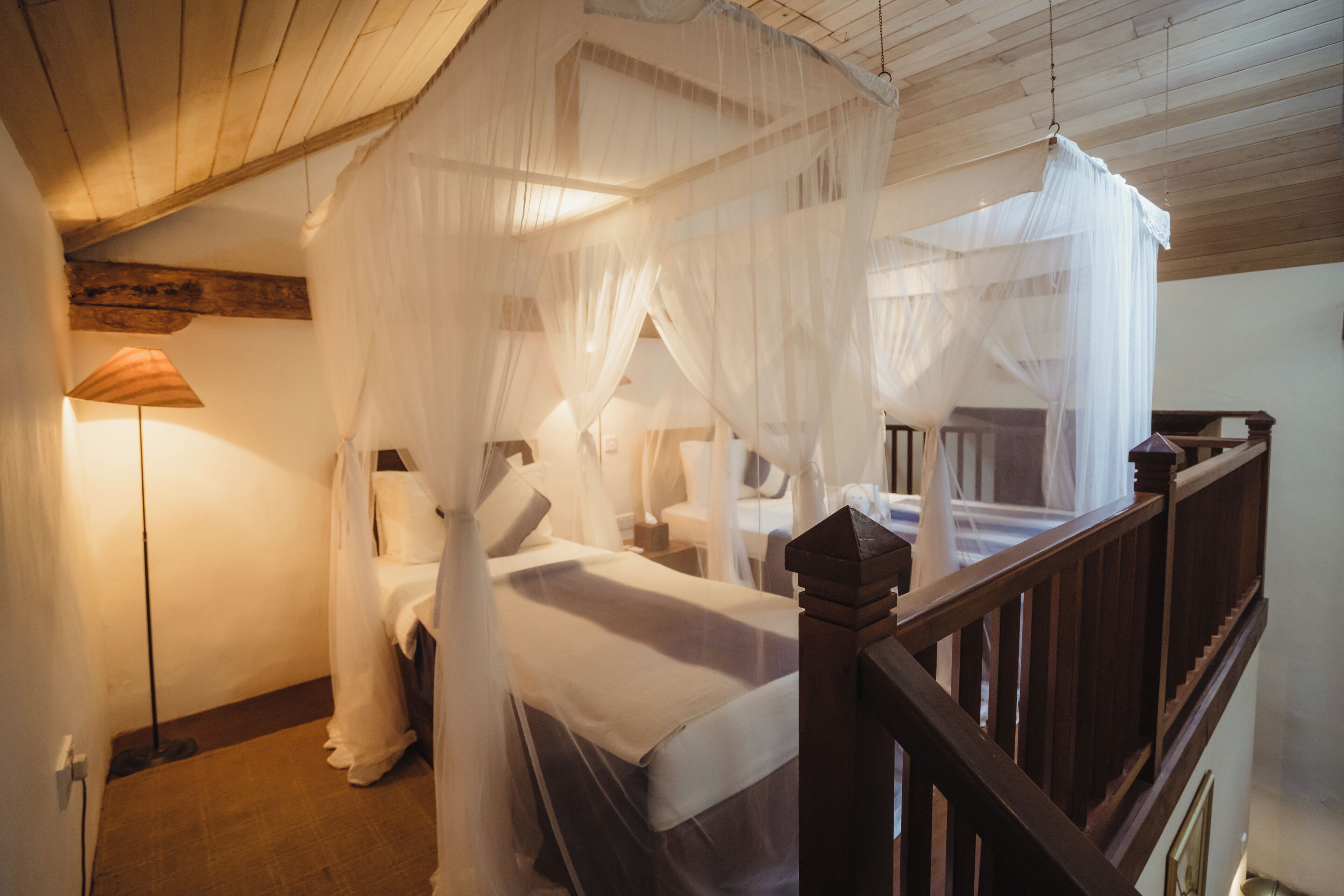 Un dormitorio con cama con dosel, vigas de madera en el techo y una mesita de noche con lámpara.