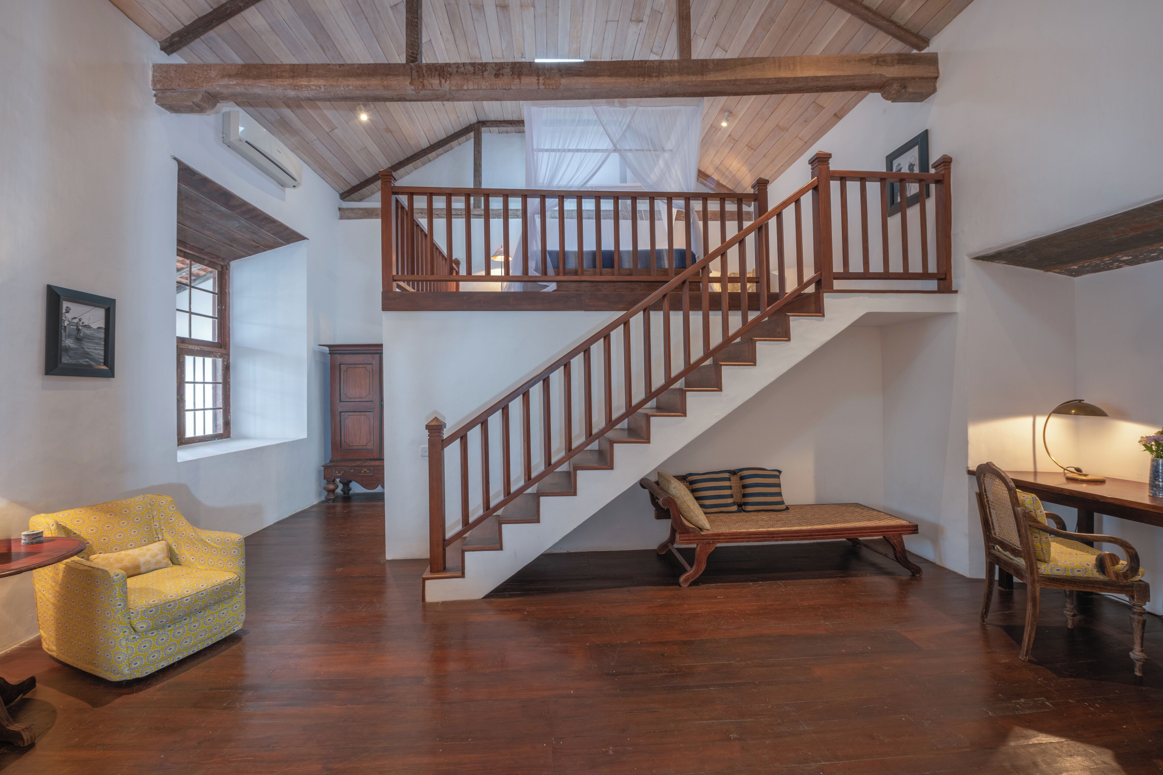 A spacious room with a wooden staircase, a sofa, a chair, and a desk.
