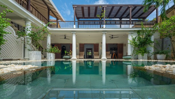 A pool with clear water, surrounded by columns and potted plants, with a covered balcony above. - 32 Middle Street (Galle)