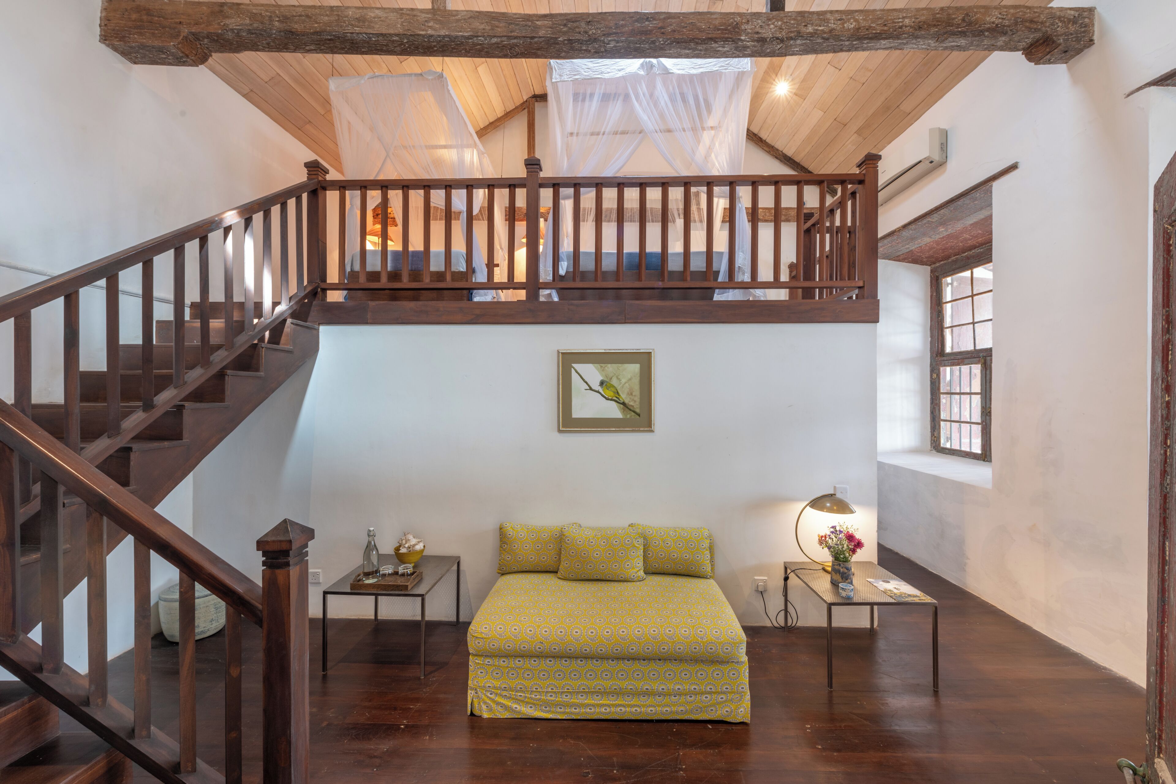 A bedroom with a wooden staircase, a bed with patterned bedding, a bedside table with a lamp, and a framed picture on the wall.