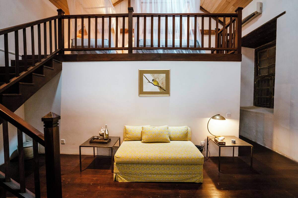A bedroom with a bed, a nightstand, a lamp, a picture on the wall, and a staircase.
