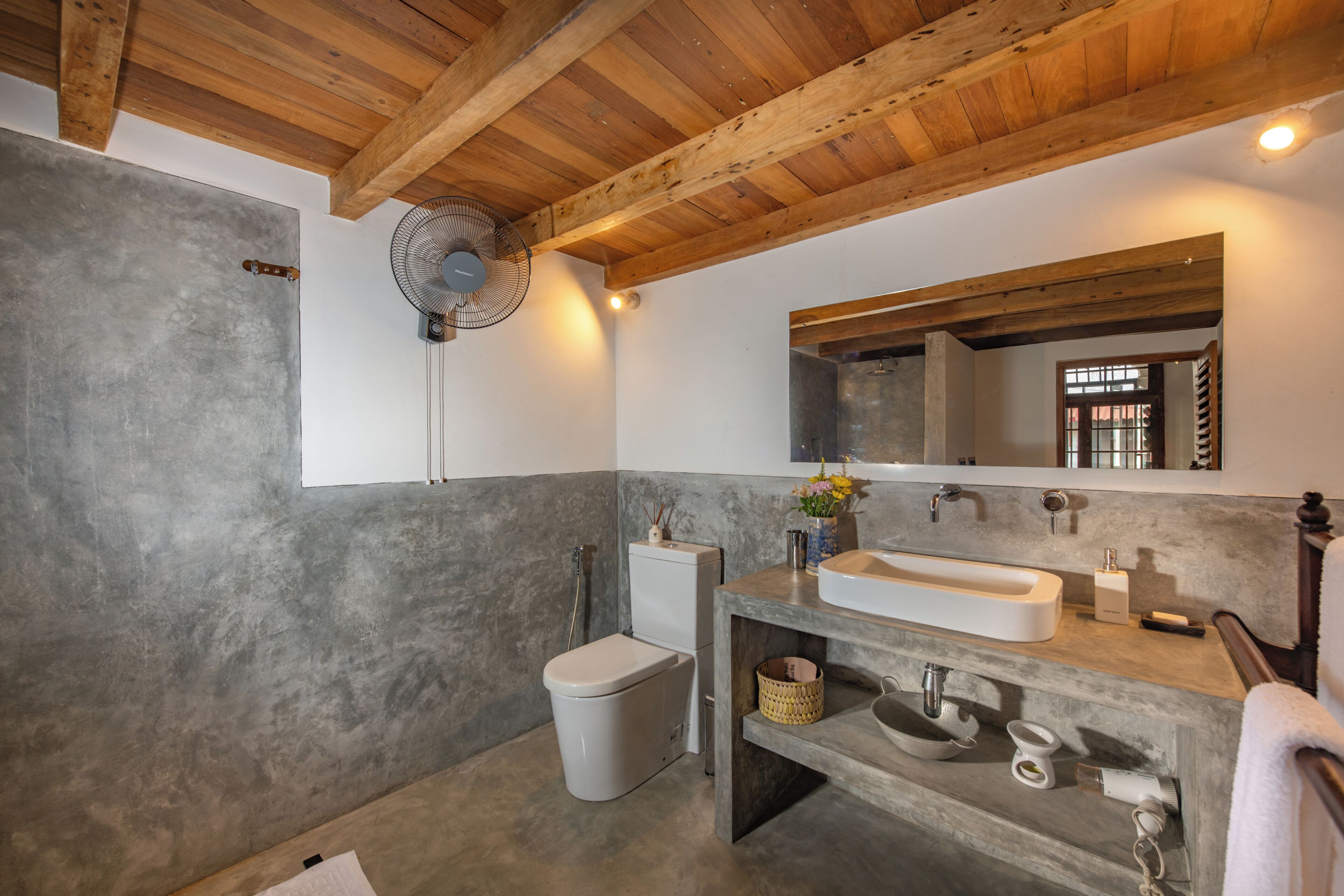 A bathroom with a wooden ceiling, a large mirror, a sink, and a toilet.