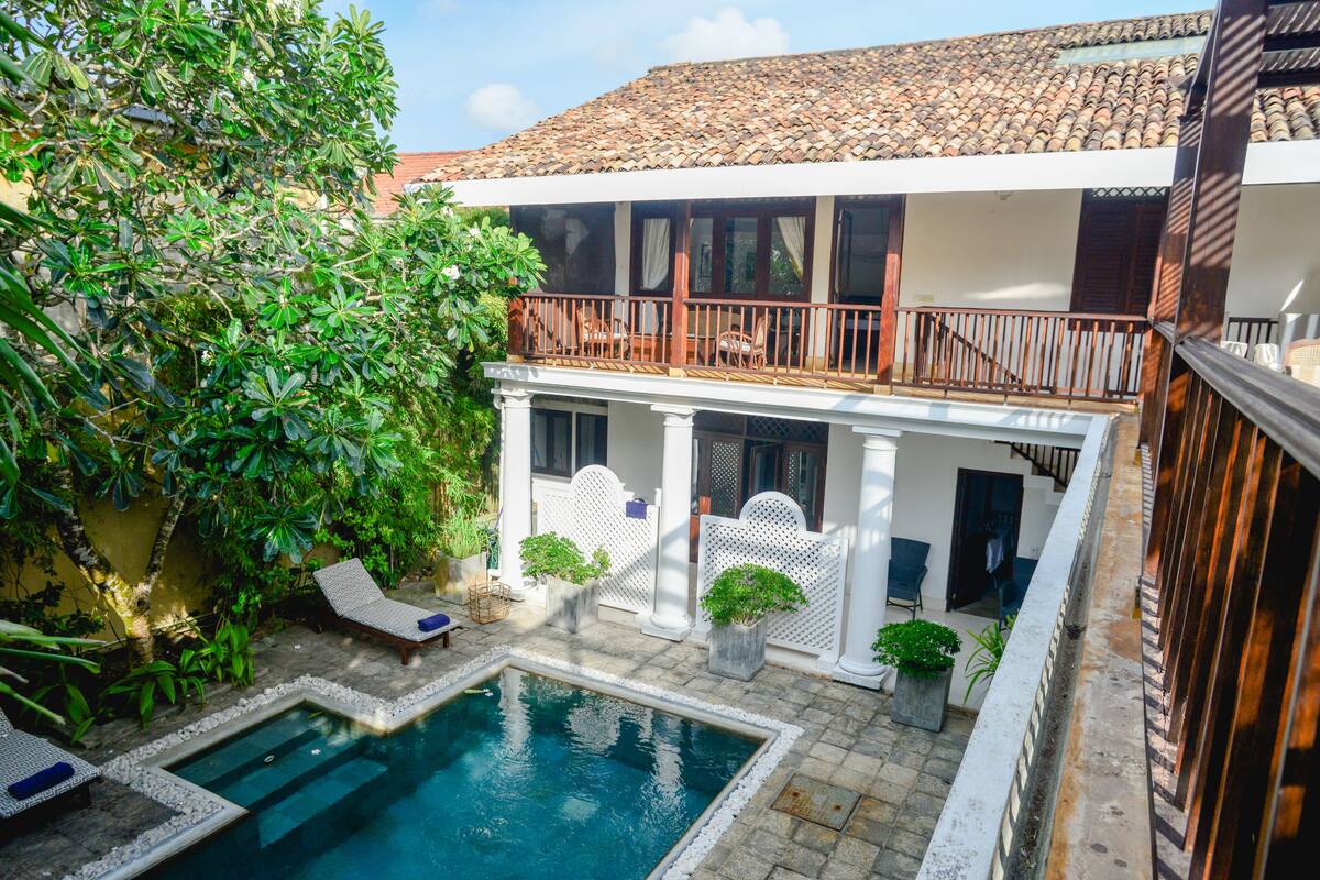 A pool area with lounge chairs, a small pool, and a covered balcony with a railing.