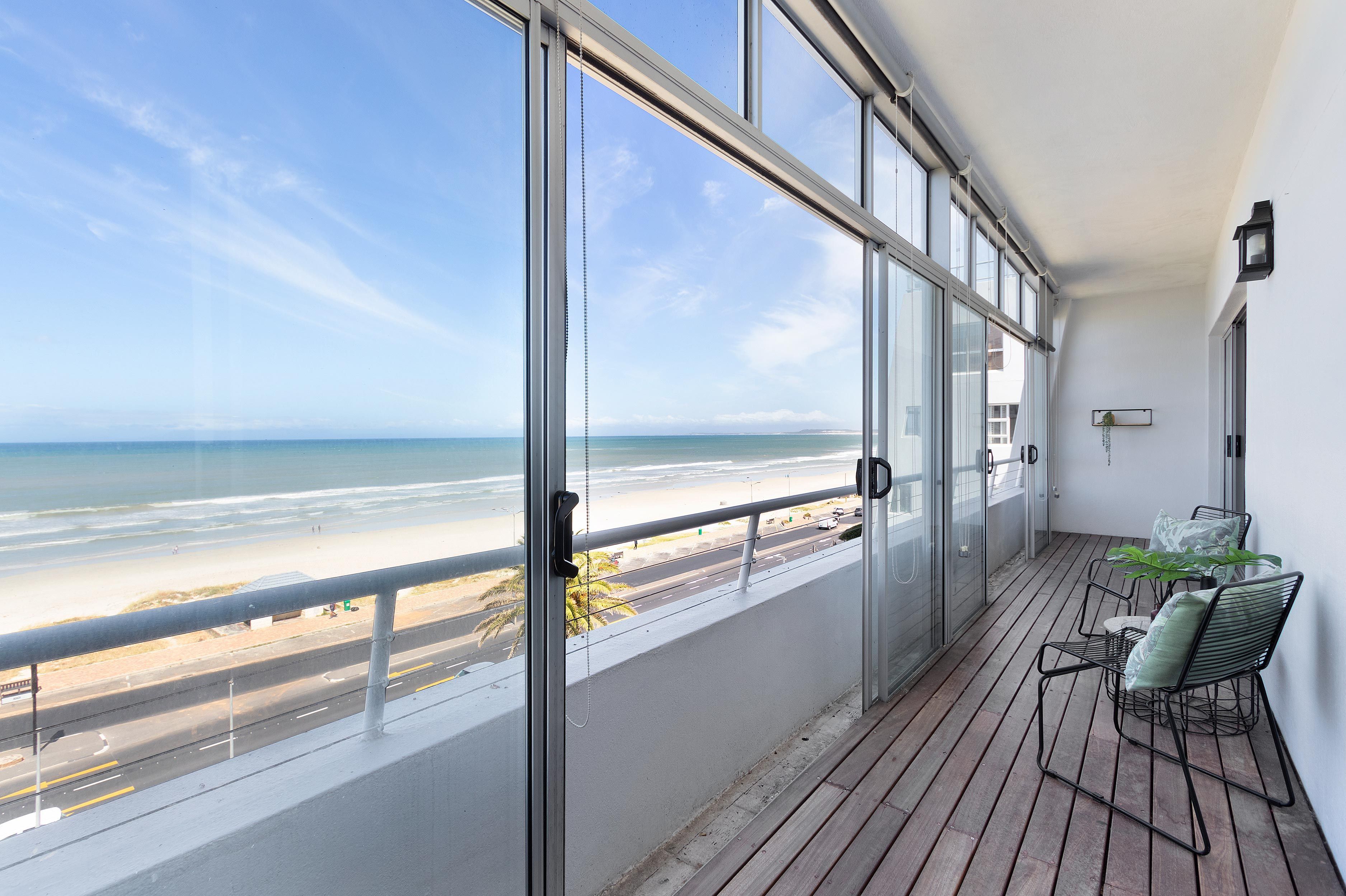 A balcony with a view of the beach, a table with chairs, and a potted plant.