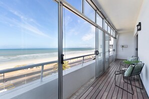 A balcony with a view of the beach, a table with chairs, and a potted plant. - Searenity (Cape Town)