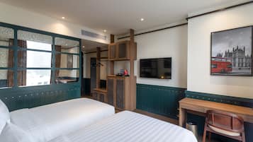 Ein Hotelzimmer mit zwei Betten, einem Schreibtisch, einem Stuhl, einem Fernseher und einem Bild eines roten Doppeldeckerbusses.