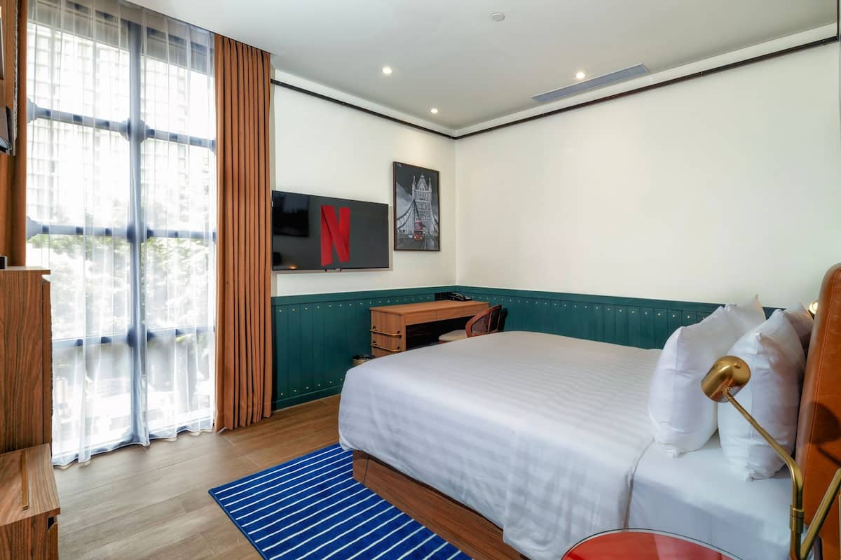 Une chambre d’hôtel avec un grand lit, un bureau, une chaise, un téléviseur fixé au mur et une fenêtre avec des rideaux.