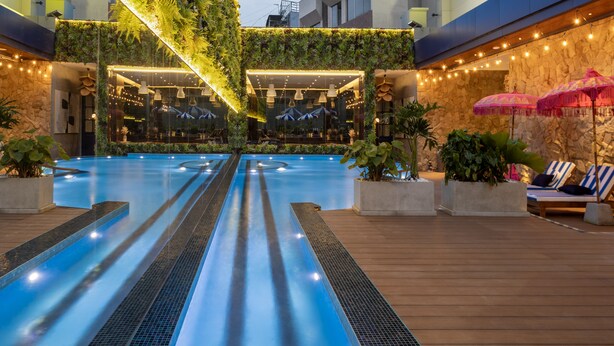 A rooftop swimming pool with a glass barrier, surrounded by lounge chairs and potted plants.
