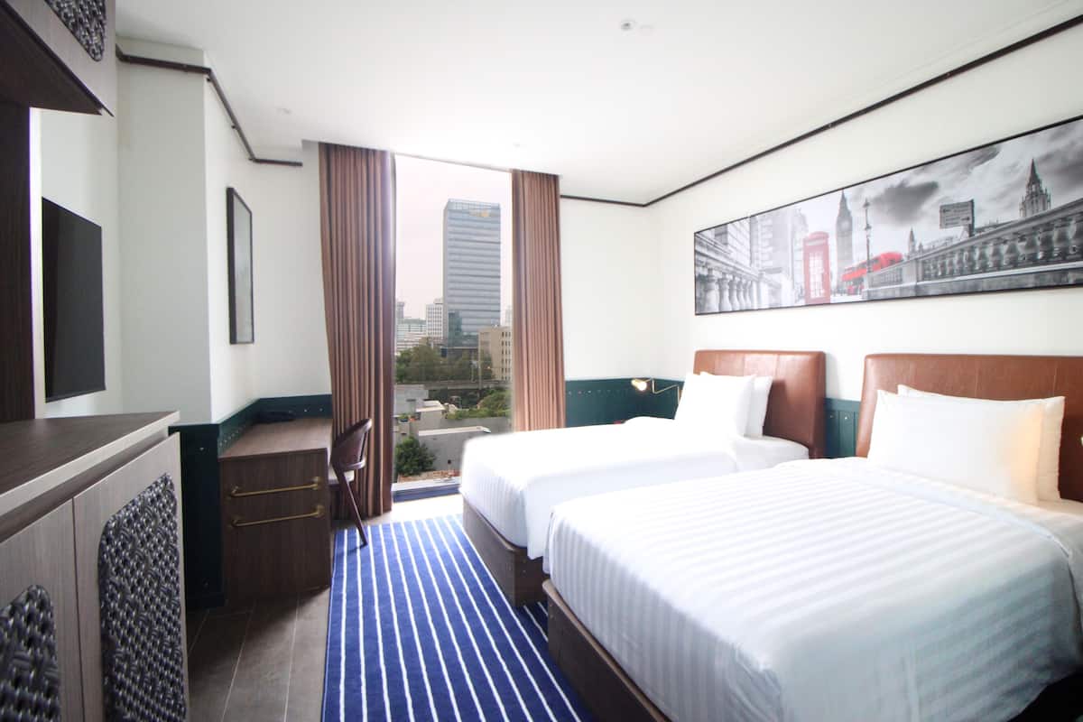 Une chambre d’hôtel avec deux lits, une télévision, un bureau et une vue sur la ville.