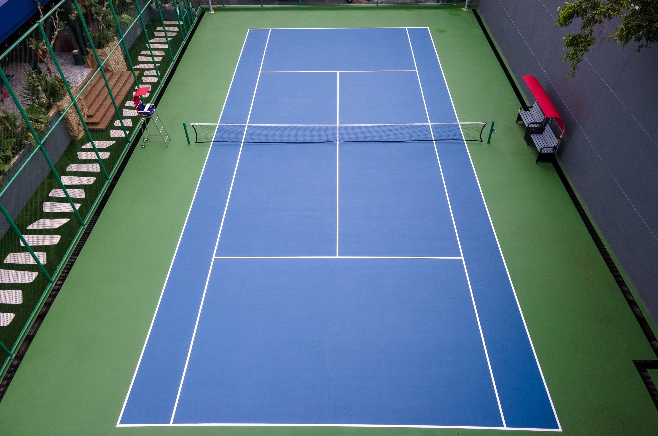 A tennis court with a net, green and blue surface, and benches along the wall.
