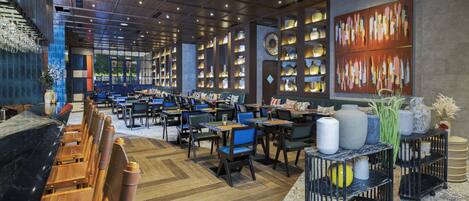A spacious restaurant with high ceilings, wooden tables and chairs, and shelves displaying various dishes.