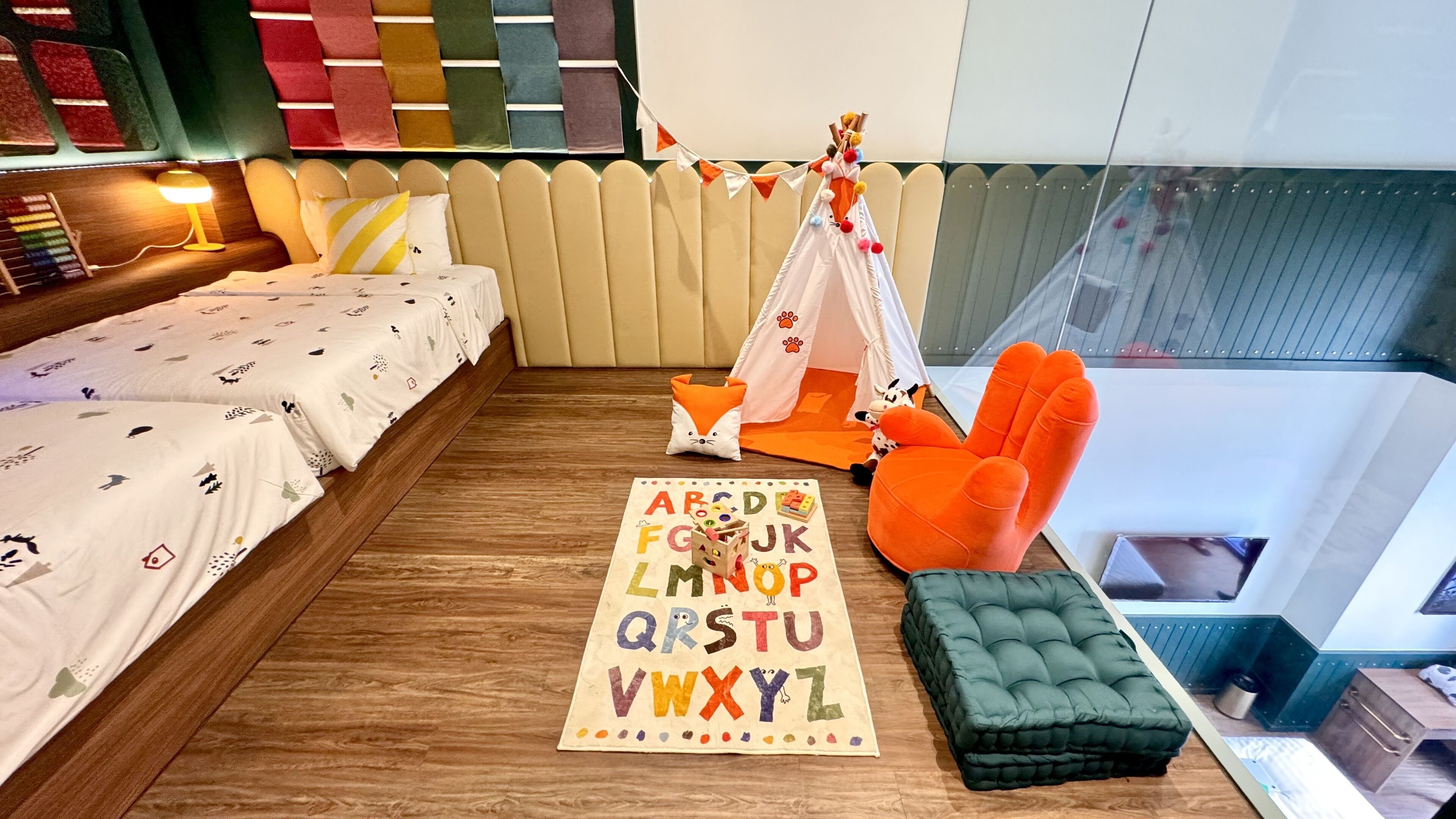 Un dormitorio acogedor con cama, una tienda de campaña pequeña, una silla y una alfombra con letras del alfabeto.